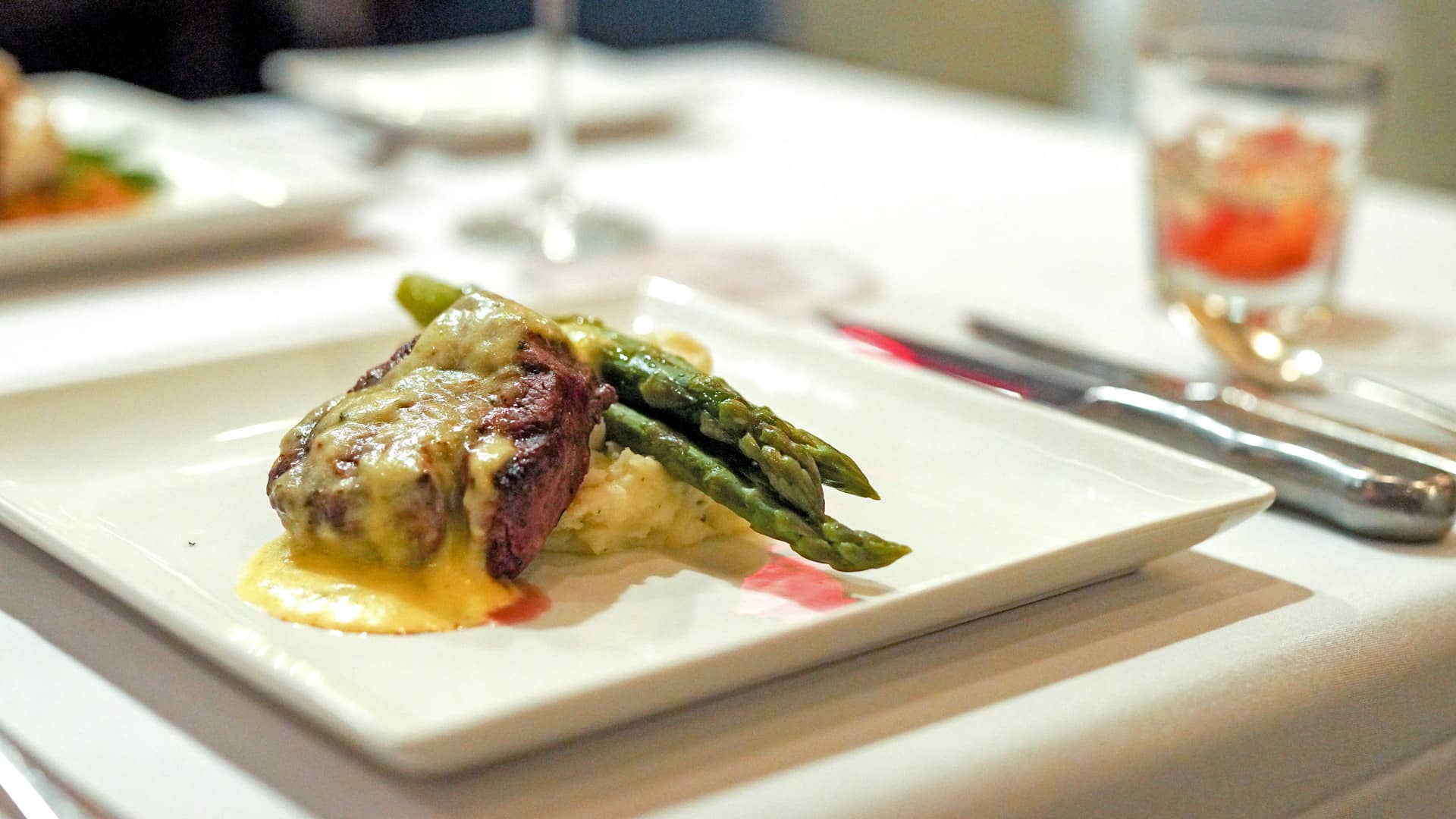 Close-up photo of catered meal from the Metropolitan Club with a steak on a bed of mashed potatoes and asparagus on a white square plate